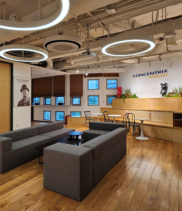 Concentrix Catalyst 오피스 라운지 — 원형 조명과 우드 인테리어가 조화를 이루는 휴식 공간